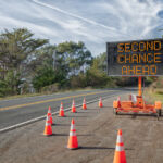 SECOND CHANCE AHEAD: This is a photograph of a mobile roadside sign parked on highway one in northern California. It is a trailer and powered by batteries and provides information and warnings for drivers by displaying words on a large panel display.