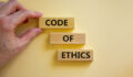 Code of ethics symbol. Wooden blocks with words 'Code of ethics'. Beautiful white background. Businessman hand. Copy space. Motivational, business and code of ethics concept.