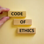 Code of ethics symbol. Wooden blocks with words 'Code of ethics'. Beautiful white background. Businessman hand. Copy space. Motivational, business and code of ethics concept.