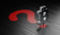Metallic Bitcoin symbol standing on red question mark over black background. Horizontal composition with selective focus and copy space.