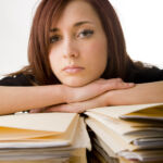 A bored looking office worker behind a large pile of files.
