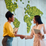 SEC and CFTC pledge to cooperate, including on exams Two diverse businesswomen shaking hands, celebrating a successful business deal in a modern office featuring a unique moss wall map, embodying collaboration and mutual respect