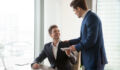 General manager presenting an envelope with premium or bonus cash to male company official. Boss congratulating happy employee with career promotion, thanking for good job and giving financial reward