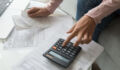 Close up cropped image coffee table full with papers invoices cheque bills, female hands holding receipt calculating company expenses results of incomes, bookkeeper accountant doing paperwork concept