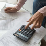 Close up cropped image coffee table full with papers invoices cheque bills, female hands holding receipt calculating company expenses results of incomes, bookkeeper accountant doing paperwork concept