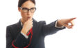 Waist up image of a business woman blowing a whistle and pointing. Concept for corporate whistle blower or industry regulator. She is dressed in formal business attire. Studio shot on a white background.