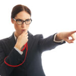 Waist up image of a business woman blowing a whistle and pointing. Concept for corporate whistle blower or industry regulator. She is dressed in formal business attire. Studio shot on a white background.