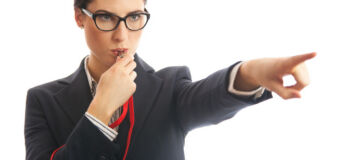 Waist up image of a business woman blowing a whistle and pointing. Concept for corporate whistle blower or industry regulator. She is dressed in formal business attire. Studio shot on a white background.