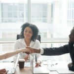 Smiling african businessman handshaking greeting caucasian businesswoman at group meeting negotiation, black satisfied entrepreneur welcoming partner shaking hand in lawyers office, respect concept
