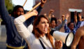 Young displeased woman using megaphone and shouting while protesting with group of people on city streets.