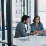 Business man, woman and laptop in discussion for deal, agreement and proposal for b2b collaboration. People, computer and meeting with paperwork for financial strategy, stats or negotiation in office