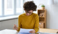 Serious concentrated young woman in glasses sitting at table and analyzing tax documents in home office