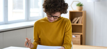 Serious concentrated young woman in glasses sitting at table and analyzing tax documents in home office