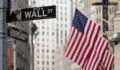 Wall street sign in New York City with American flags and New York Stock Exchange in background.