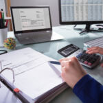 Close-up Of A Businessperson's Hand Calculating Invoice At Workplace