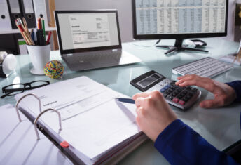 Close-up Of A Businessperson's Hand Calculating Invoice At Workplace