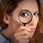 Headshot woman investigator looking through magnifying glass