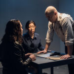 A police detective at the station and his partner, an Asian woman, present evidence to a male suspect in an interview room
