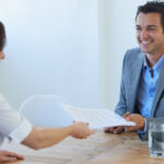 A smiling businessman receiving a resume from a young woman at a job interview