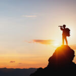 vision for success ideas. businessman's perspective for future planning. Silhouette of man holding binoculars on mountain peak against bright sunlight sky background.