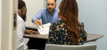 The diverse couple meet with their banker to sign loan paperwork for their new car.