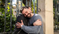 SEC/CFTC request comment on the swap definitions and on alternative compliance Two adult brothers enjoy a warm embrace in a sunny park. They stand beside a decorative fence surrounded by lush greenery, showcasing a strong bond and happiness in the moment.
