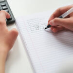 A student doing math in a notebook using a calculator. Close up.