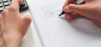 A student doing math in a notebook using a calculator. Close up.