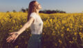 Beautiful smiling redhead enjoying a carefree summer day in a yellow flower field.