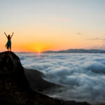 Woman enjoys on top of a cliff above the sea of clouds at sunset.