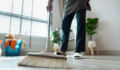 A person cleaning the floor with a broom in a bright, modern home interior featuring houseplants and natural light.