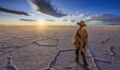 Female tourist, wearing a traditional hat and poncho, admires the sunset at Salar de Uyuni, Altiplano, Bolivia. Salar de Uyuni (or Salar de Tunupa) is the world's largest salt flat at 10,582 square kilometers (4,086 sq mi). It is located in the Potosi and Oruro departments in southwest Bolivia, near the crest of the Andes, and is elevated 3,656 meters above the mean sea level. The Salar was formed as a result of transformations between several prehistoric lakes.