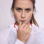 Whistleblower reaction: Speed things up Portrait of young beautiful woman with whistle and serious expression. Isolated white background.