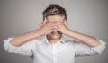 Closeup portrait young male, shy man closing covering eyes with hands can't see, hiding, isolated grey wall background. See no evil concept. Negative human emotion, facial expression, feeling reaction