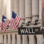 Wall Street sign with the blurred flags of the stock exchange as background. October 2017