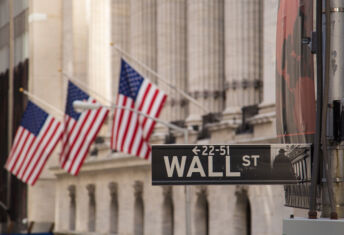 Wall Street sign with the blurred flags of the stock exchange as background. October 2017