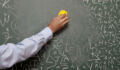 Human hand erasing blackboard with large amount of letters written on.His hand is entering to frame from left side of photo.He is holding a yellow eraser.Large amount of letters are written on green blackboard.Part of hand is in frame.The model is unrecognizable.Photo was shot with a full frame DSLR camera.