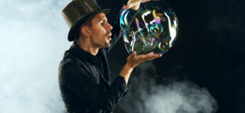 Man artist blowing many soap bubble. Soap bubble show in black studio.