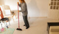 Woman performing household chores, sweeping tiled floor with a red broom in her home