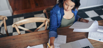 Shot of a young woman using a laptop and going through paperwork while working from home