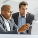 African American businessman and his colleague cooperating while reading an e-mail on a computer in the office.