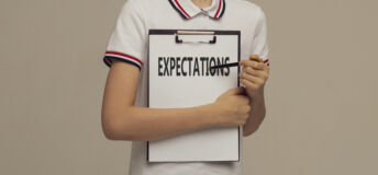 A young man in a white polo is holding a clipboard and pointing with a pen at a word Expectations, Business, technology, internet concept. Stock Image.