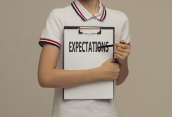 A young man in a white polo is holding a clipboard and pointing with a pen at a word Expectations, Business, technology, internet concept. Stock Image.