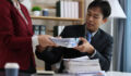 Employees exchanging a stack of business documents in a modern office, showing collaboration and administrative tasks