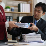 Employees exchanging a stack of business documents in a modern office, showing collaboration and administrative tasks